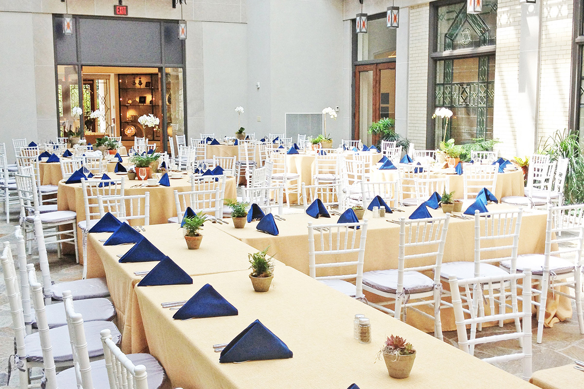 Event space with banquet tables and white chairs arranged for a reception or gathering in a bright indoor atrium.