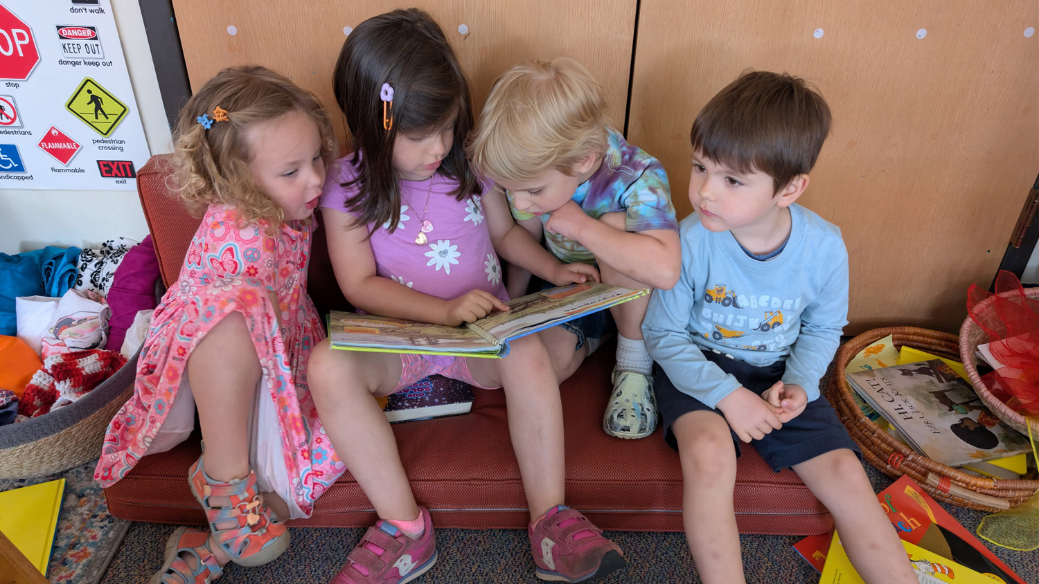 Children gathered together reading a book in a classroom reading corner surrounded by books and learning materials.