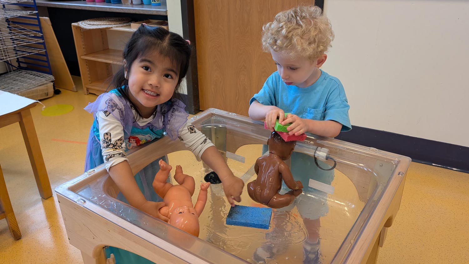 Children engaged in water play at a classroom sensory table.
