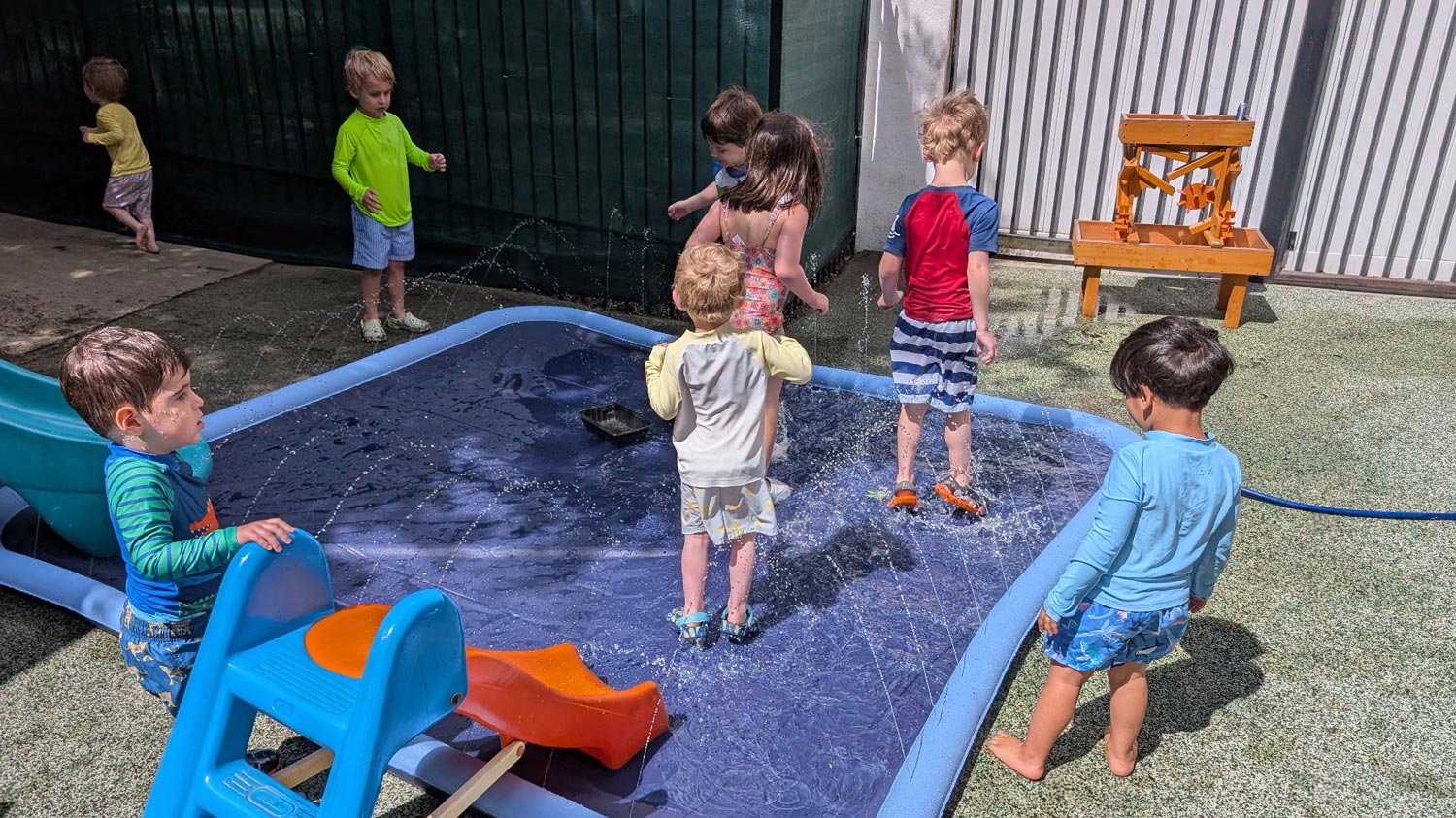 Children playing in a shallow splash pool and water play area during an outdoor summer camp activity.