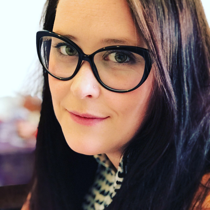 Professional headshot of a staff member wearing dark-framed glasses against a softly blurred background.