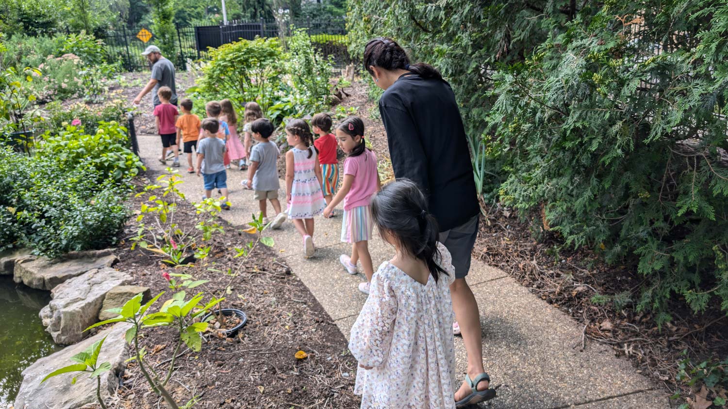 Children and educators walking together along a garden path during an outdoor exploration activity.