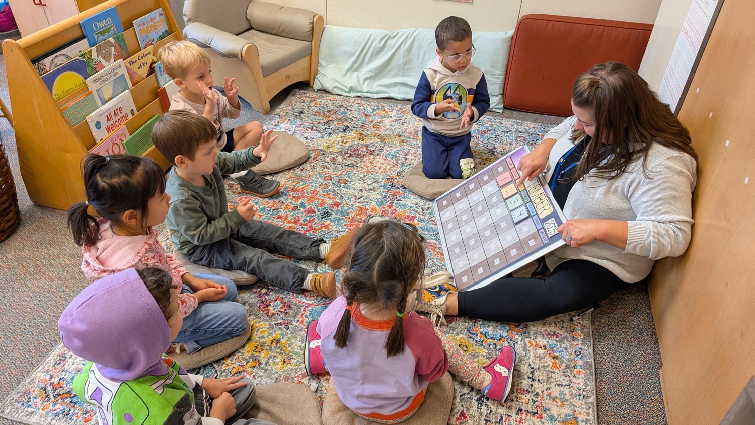 Teacher leading a small group learning activity with preschool children seated together on a classroom rug.