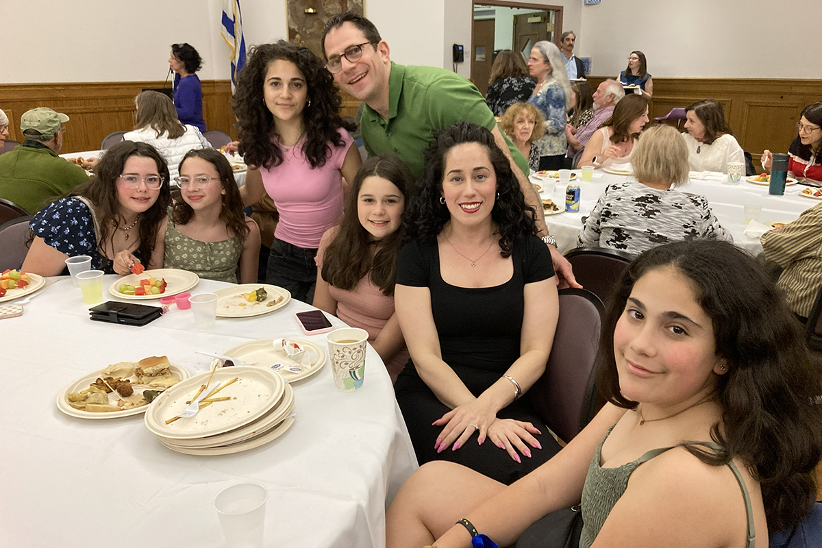 Adults and children gathered around a table after Shabbat dinner.